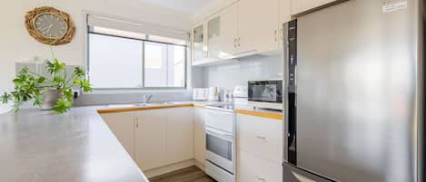 Eine moderne Küche mit einem Edelstahl-Kühlschrank, eingebautem Backofen, Mikrowelle und einem großen Fenster für natürliches Licht.
