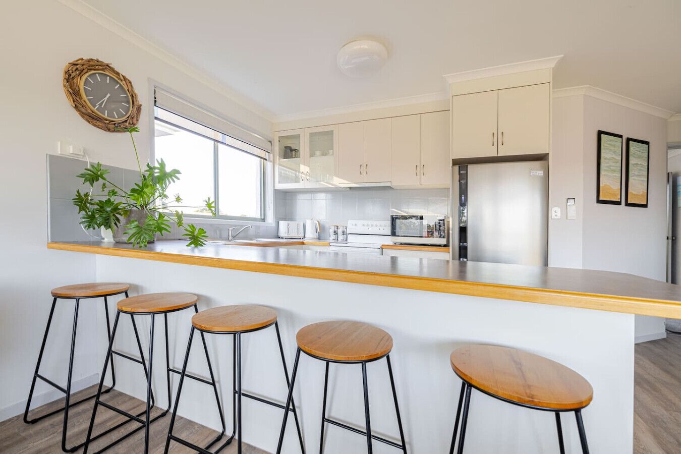 Una cocina moderna con armarios blancos, un refrigerador de acero inoxidable, una barra de madera y cuatro taburetes de bar.