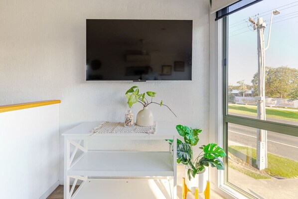 Ein Zimmer mit einem weißen Tisch, einem an der Wand befestigten Flachbildfernseher und Blick auf die Straße durch ein großes Fenster.