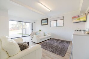 Ein modernes Wohnzimmer mit einem weißen Sofa, einem grauen Teppich und einer Küchenzeile mit Arbeitsplatte und Spüle.