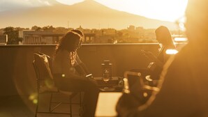 Dos personas sentadas a una mesa con una copa de vino, con vistas a un paisaje urbano y montañas al fondo.