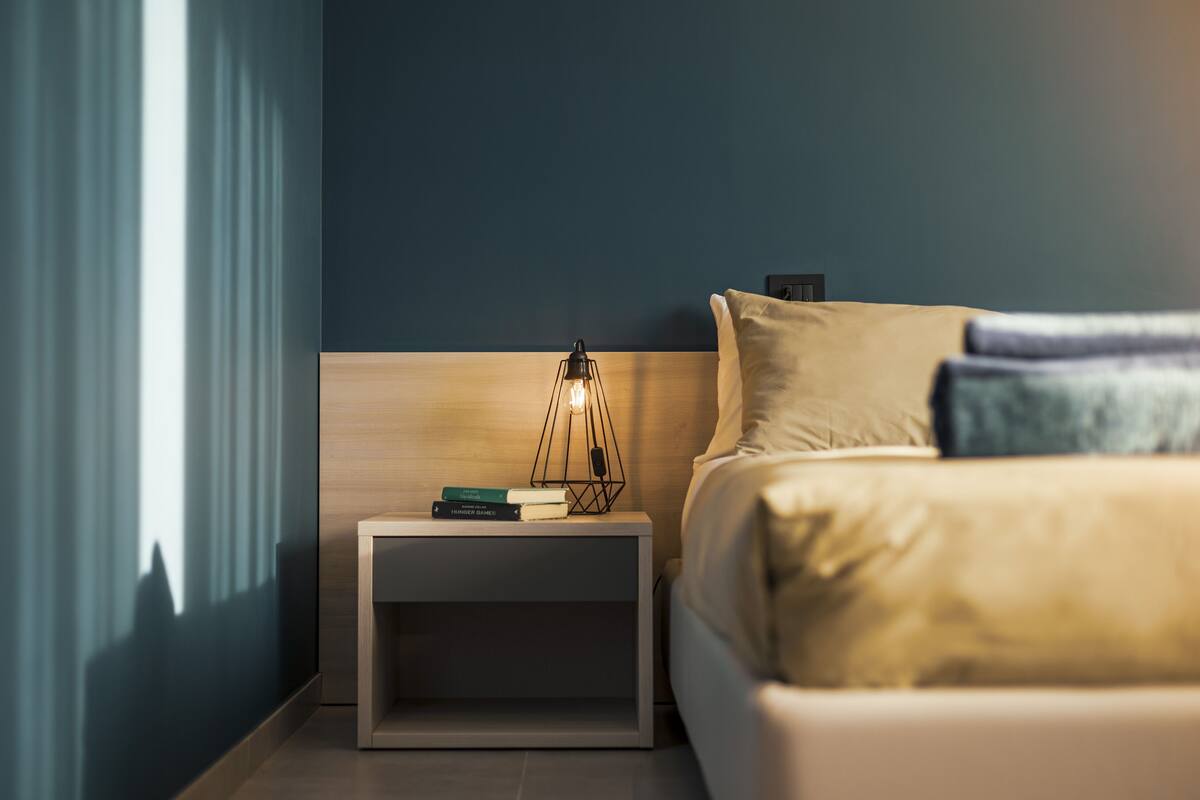 Un lit bien fait, avec une tête de lit, une table de chevet avec une lampe et une petite table de nuit avec des livres.