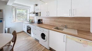 A modern kitchen with white cabinets, a wooden countertop, a built-in washing machine, and a window providing natural light.