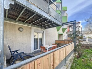 A covered outdoor patio with a table and chairs, a wooden fence, and a building with a green and white facade in the background.