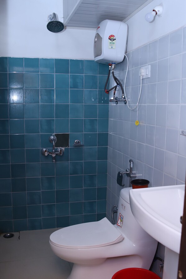 A bathroom with a white toilet, a shower head, and a white sink. - Hotel Pine Tree (Rajkot)