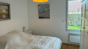 Une chambre à coucher avec un lit, un tableau, une lampe, une fenêtre donnant sur un paysage verdoyant et un luminaire au plafond.