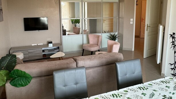 Ein modernes Wohnzimmer mit einer Couch, Sesseln, einem Fernseher und einer Schiebetür zu einem Balkon.
