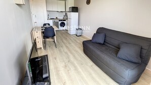 A compact living space with a sofa, a dining area, a kitchen, and a washing machine. - 1-Bedroom Apartment 100m from Beach - Sleeps 4, Air Conditioning, Nearby Parking (Argelès-sur-Mer)