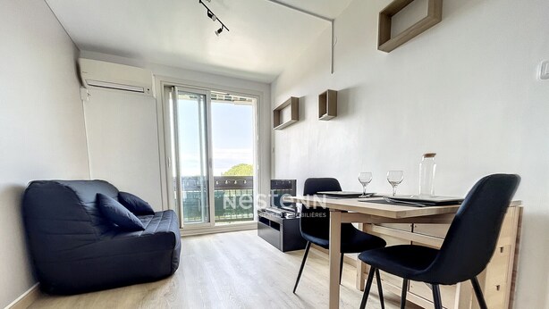 A modern living room with a black sofa, a wooden dining table with chairs, and a sliding glass door leading to a balcony. - 1-Bedroom Apartment 100m from Beach - Sleeps 4, Air Conditioning, Nearby Parking (Argelès-sur-Mer)