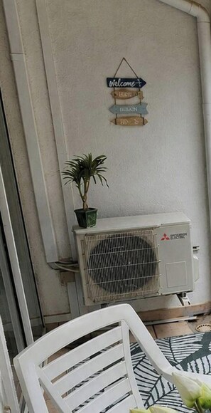 Una stanza con una sedia bianca, una pianta in vaso e un condizionatore Mitsubishi.