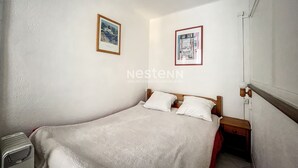 A small, neatly arranged bedroom with a bed, two bedside tables, and two framed pictures on the wall. - Cozy T2 Apartment with Terrace, 400m from the Beach (Argelès-sur-Mer)