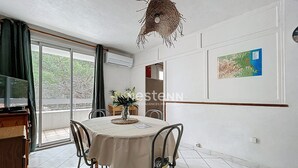 A dining area with a round table, chairs, a vase with flowers, a hanging light fixture, and a map on the wall. - Cozy T2 Apartment with Terrace, 400m from the Beach (Argelès-sur-Mer)