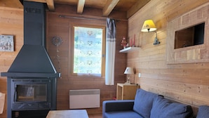 A cozy cabin interior with a wood-burning stove, a sofa, a table, and a window with curtains.