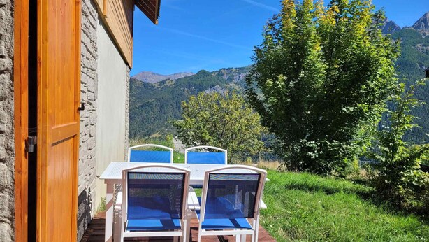 A wooden deck with a table and chairs, overlooking a mountainous landscape.