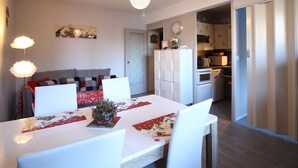 Un comedor con una mesa y sillas blancas, una araña y una cocina al fondo.
