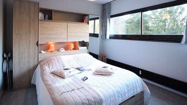 Un dormitorio moderno con una cama grande, estanterías empotradas, una mesita de noche y una ventana con vistas a árboles.