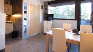 Una habitación compacta con una mesa de comedor, sillas, televisor y una zona de cocina con refrigerador y armarios.
