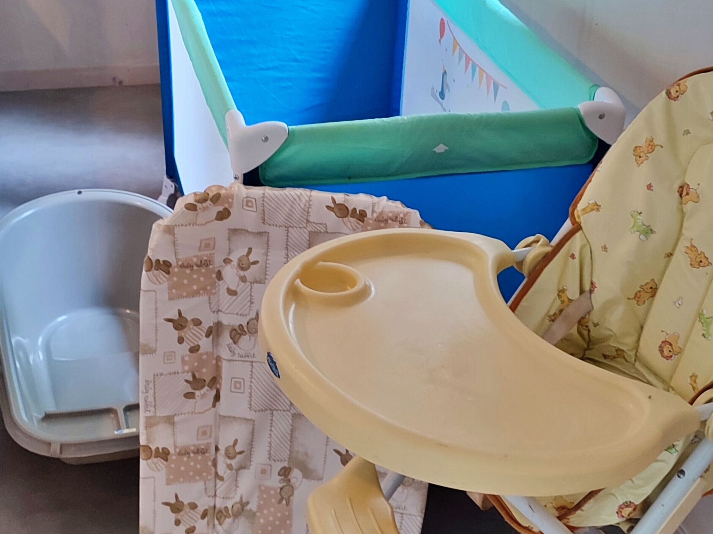 Un cambiador para bebés con asiento acolchado azul y verde, una bandeja blanca y un paño estampado.