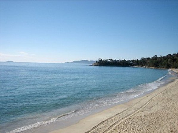 A beach with clear blue water, sandy shore, and a distant landmass with trees.