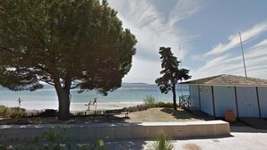 A beachside property with a large tree, a small building, and a view of the sea. - Cozy Ground Floor Studio in Cavalière with Sunny Terrace, Close to Beach & Shops (Le Lavandou)