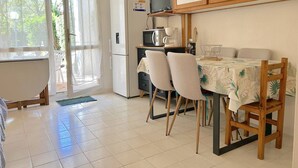 A compact kitchen with a refrigerator, microwave, and coffee maker, a dining table with chairs, and a view through a window. - Cozy Ground Floor Studio in Cavalière with Sunny Terrace, Close to Beach & Shops (Le Lavandou)