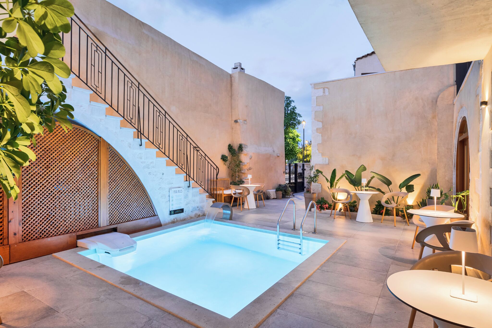 A pool area with a staircase, outdoor seating, and plants.