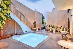 A pool area with a staircase, outdoor seating, and plants.