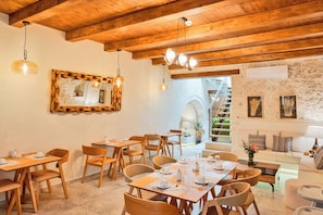 A cozy dining area with wooden tables and chairs, a stone wall, and a staircase leading to an upper level.