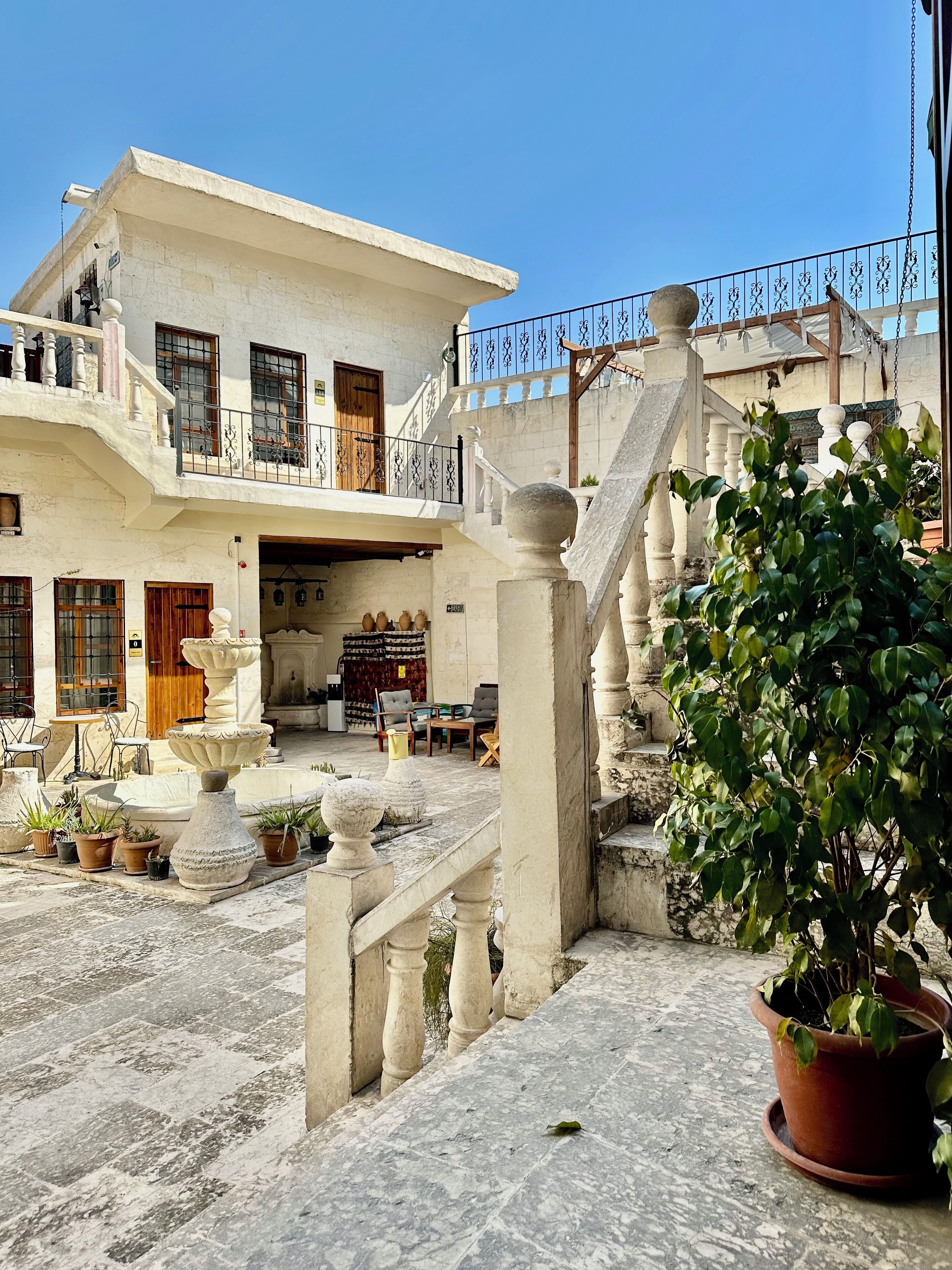 A courtyard with a fountain, potted plants, and a staircase leading to an upper level.