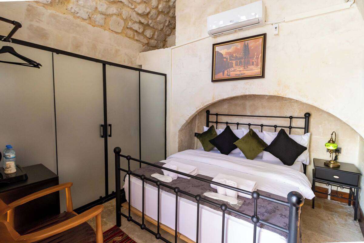 A bedroom with a bed, a wooden chair, a nightstand, a lamp, and a framed picture on the wall.