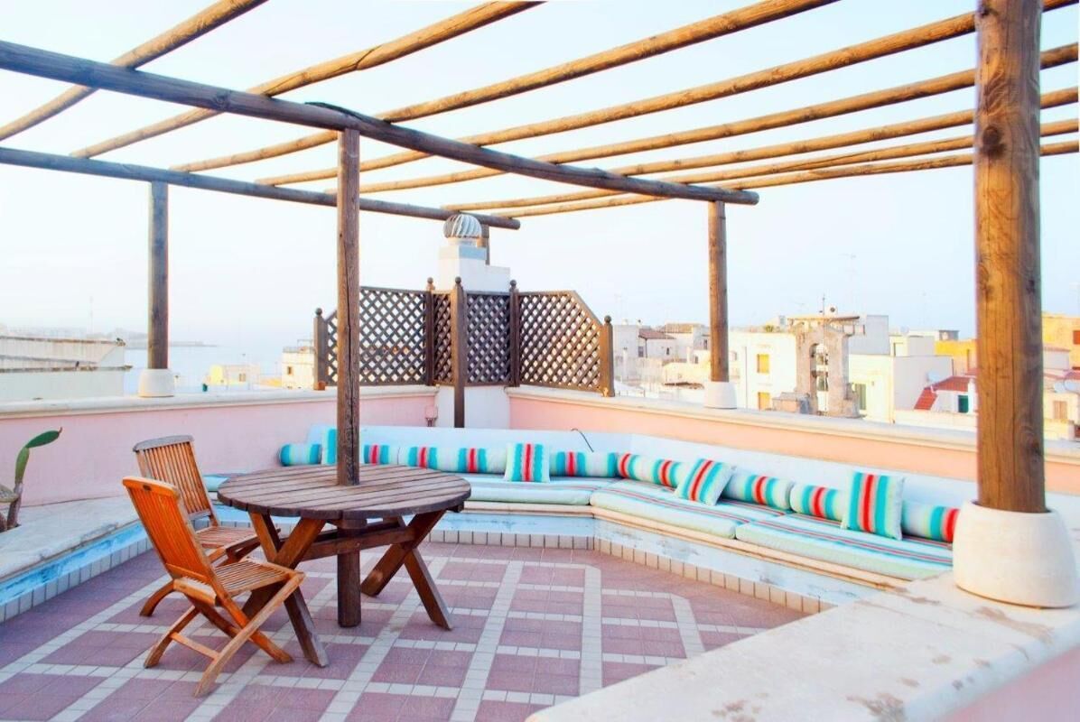A rooftop terrace with a wooden pergola, a round table, and a curved seating area with colorful cushions.