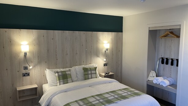 A hotel room with a bed, bedside tables, a hanging clothes rack, and a towel rack. - The White Horse (Driffield)