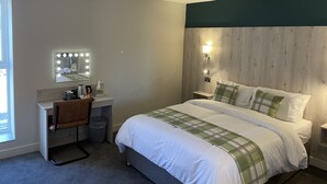 A hotel room with a bed, a vanity with a mirror and lights, a desk, and a window. - The White Horse (Driffield)