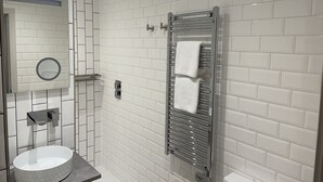 A modern bathroom with white subway tiles, a round mirror, a white sink, and a glass shower enclosure with a towel rack. - The White Horse (Driffield)