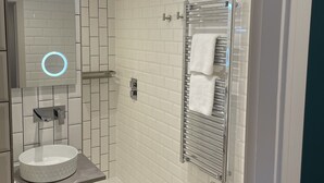 A modern bathroom with a white tiled wall, a round mirror with a light, a white sink, and a towel rack. - The White Horse (Driffield)
