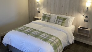 A neatly made bed with a plaid bedspread, two bedside tables with lamps, and a wooden headboard. - The White Horse (Driffield)