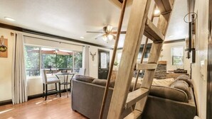 Un vaste salon agrémenté d’un escalier en bois, un coin repas avec une table et des chaises, et une grande fenêtre offrant une vue sur l’extérieur.