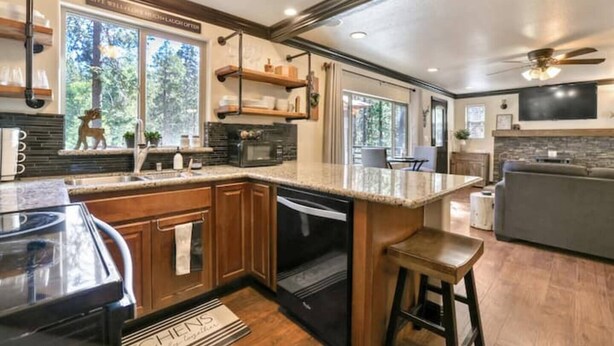 Une cuisine moderne dotée de plans de travail en granit, d’armoires en bois et d’un grand îlot central. On y trouve des appareils électroménagers intégrés, un coin bar et un espace repas bien visible.
