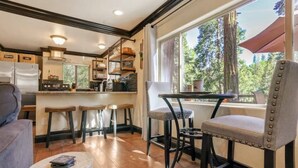 Une cuisine chaleureuse avec un plancher en bois, un coin repas avec une table et des chaises, et une grande fenêtre donnant sur les arbres.