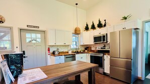 Une cuisine moderne avec des meubles blancs, un réfrigérateur en acier inoxydable, un four à micro-ondes et une table à manger en bois, accompagnée de tabourets.