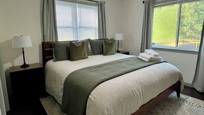 Une chambre d’hôtel avec un lit, deux lampes de chevet, une fenêtre avec des rideaux et une vue sur la verdure.