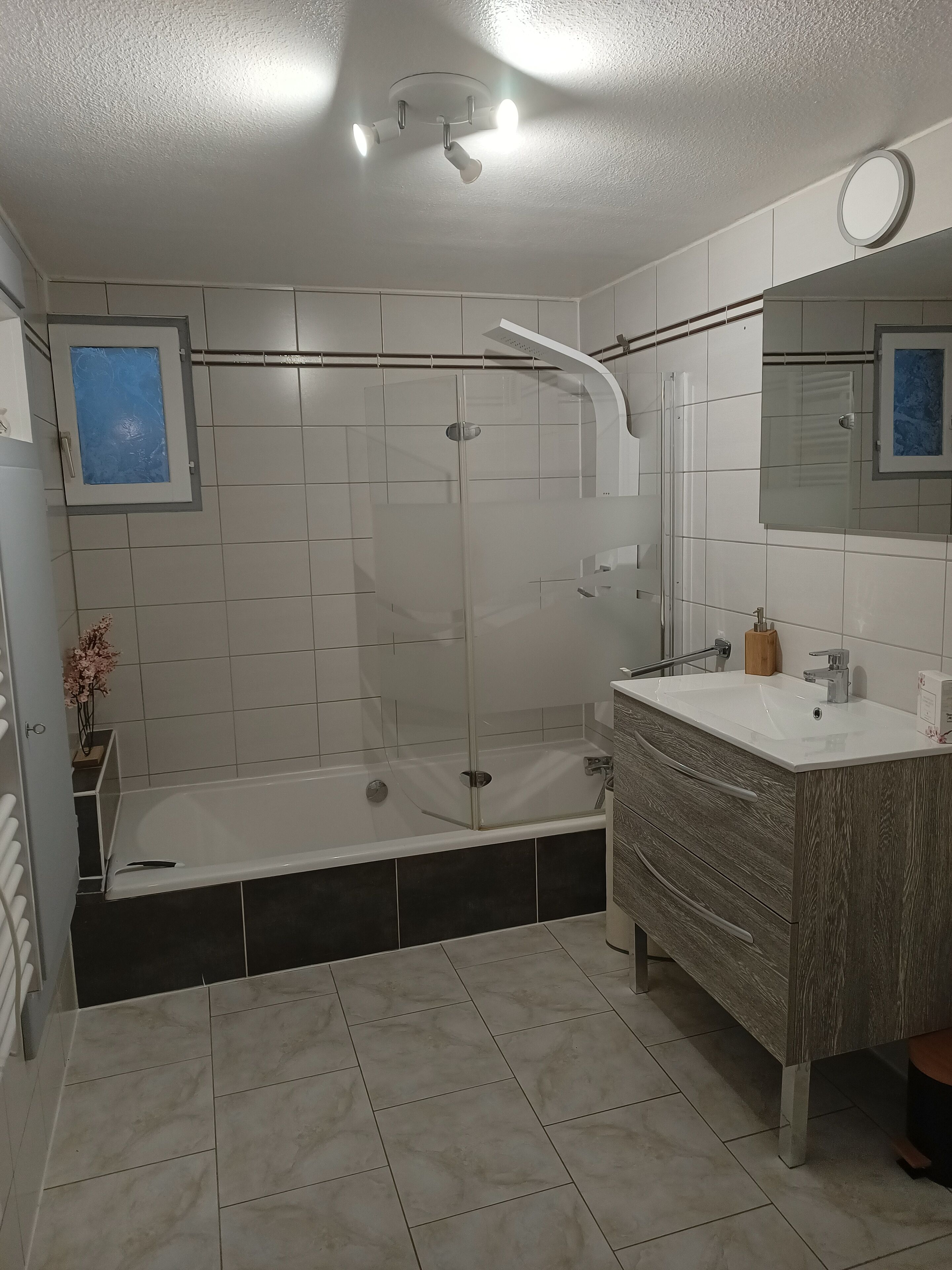 A modern bathroom with a glass-enclosed shower, a vanity with a mirror, and a tiled floor.