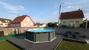A swimming pool with a wooden deck, surrounded by a stone wall and a grassy area. - Gîte "chez L'oncle Paul" (Urschenheim)