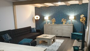 A modern living room with a dark sofa, a wooden dining table, and a light-colored rug. There are two floor lamps and a decorative vase on a cabinet. - Gîte "chez L'oncle Paul" (Urschenheim)