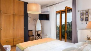 A bedroom with a bed, wooden wardrobe, a television, a mirror, and a balcony with a view. - Zen Serenity Retreat (Chania)