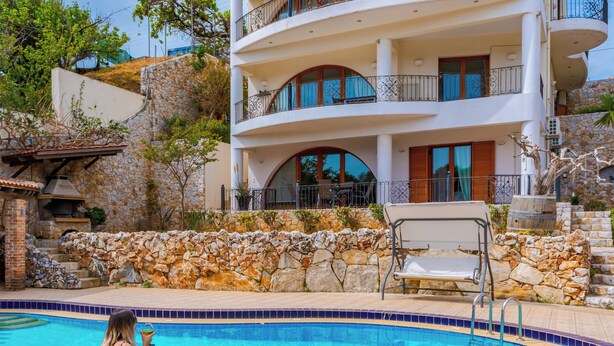A multi-story building with balconies, a swimming pool, and a stone wall. - Zen Serenity Retreat (Chania)
