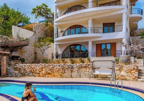 A multi-story building with balconies, a swimming pool, and a stone wall. - Zen Serenity Retreat (Chania)