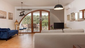 A living room with a sofa, a TV, and a balcony with a view of trees. - Zen Serenity Retreat (Chania)