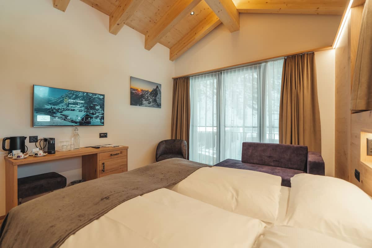 A hotel room with a bed, a desk with a computer, a TV, and a window with curtains.