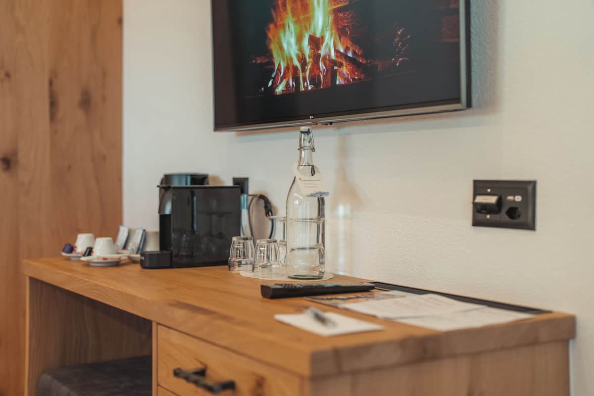 A wooden desk with a coffee maker, a glass bottle, and a remote control.
